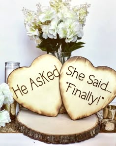 two wooden hearts with the words he asked she said finally on them next to some flowers