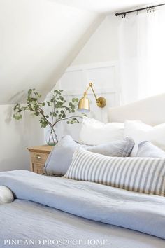 a bed with white sheets and pillows in a bedroom under a slanted ceiling light