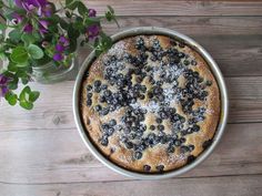 a cake with blueberries and powdered sugar sits on a table next to purple flowers