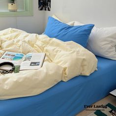 an unmade bed with blue sheets and pillows on it, next to a window