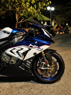 a blue and white motorcycle parked on the side of the road at night with trees in the background