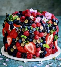 a cake with berries, strawberries and blueberries on top is surrounded by flowers