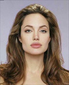 a woman with long brown hair and blue eyes posing for a photo in front of a gray background