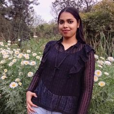 a woman standing in front of flowers with her hands on her hips and looking at the camera