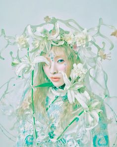 a woman with white flowers on her head and veil over her face is surrounded by green leaves