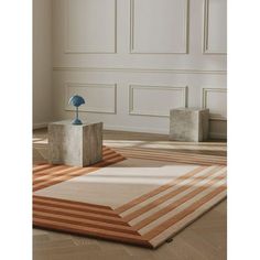 an area rug with two small sculptures on the floor in front of white paneled walls