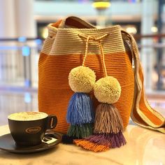 an orange purse with two tassels and a cup of coffee on the table