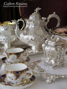 a table topped with lots of fancy tea cups and saucers on top of a white table