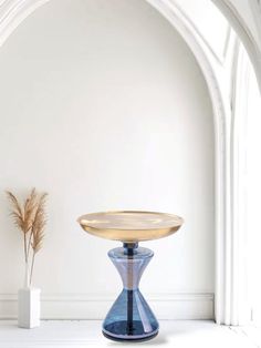 a blue vase sitting on top of a white table next to a tall brown plant