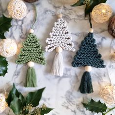 crochet christmas tree ornaments are displayed on a marble surface with greenery and lights