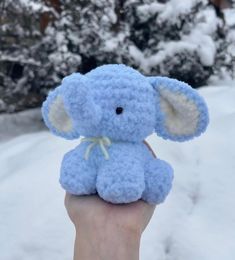 a small blue stuffed elephant sitting on top of someone's hand in the snow