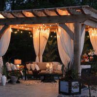 an outdoor living area with white curtains and lights