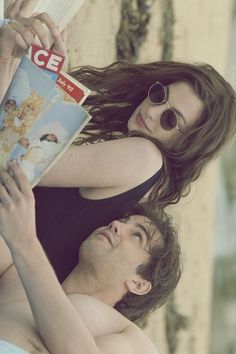 a man and woman laying on top of each other holding a book in their hands