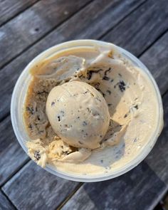 two scoops of ice cream sit in a plastic container on a wooden table top