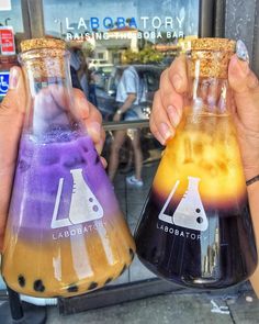 two people holding beakles filled with liquid in front of a storefront window that says labbatch laboratory