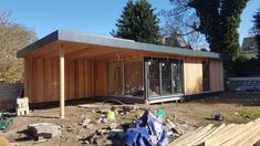 a small wooden building sitting in the middle of a yard next to a pile of wood