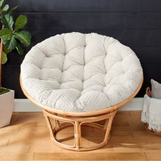 a round wicker ottoman sitting on top of a wooden floor next to a potted plant