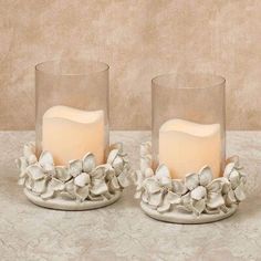 two glass candles with flowers on them sitting next to each other in front of a wall