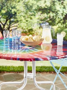 a colorful table with drinks and food on it in front of a tree filled yard