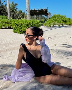 a woman sitting on top of a sandy beach next to palm trees in the sun