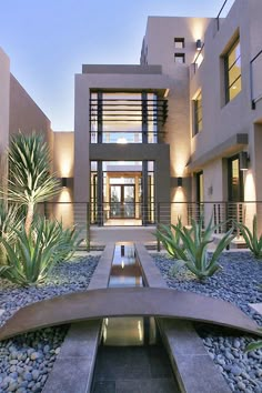 a modern house is lit up at night with lights on the windows and plants in the foreground