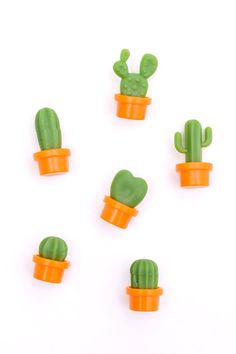 small green cactus plants in orange plastic cups on a white surface, top down view