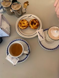 a table topped with two cups of coffee and plates filled with pastries next to each other