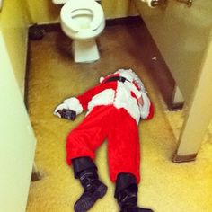 a man dressed as santa claus is laying on the floor in front of a toilet