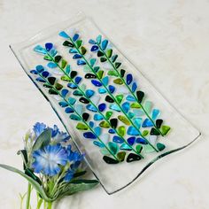 a blue flower sitting on top of a glass plate next to a vase filled with flowers