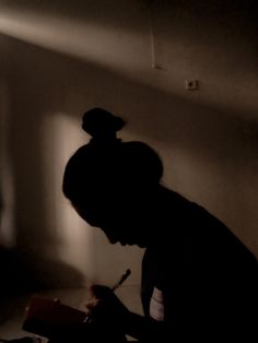 a woman writing in her dark room with the light coming through the window behind her