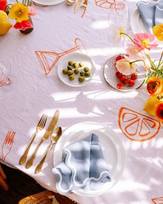 the table is set with plates, silverware and colorful flowers on it's surface