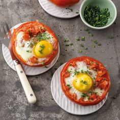 two plates topped with eggs and tomatoes on top of a table next to a knife and fork