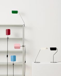 three different colored lamps sitting next to each other on a white book shelf with bookshelves in the background