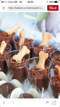 there are many desserts in plastic cups on the table and one has a dog bone sticking out of it