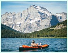 a person in an orange kayak paddling on the water with mountains in the background