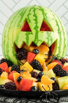 a watermelon carved to look like a jack - o'- lantern surrounded by fruit