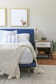 a bed with white sheets and pillows in a bedroom next to a potted plant