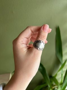 a woman's hand is holding a ring with a stone in it and a plant behind her