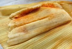 some kind of tamales sitting on top of a wooden cutting board