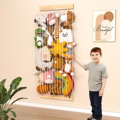 a young boy standing in front of a wall with stuffed animals hanging on it's sides