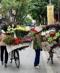 two people pushing a bicycle loaded with flowers