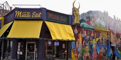 a building with many colorful murals on it's side and yellow awnings