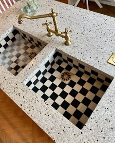 two black and white checkered tiles on the counter top next to a gold faucet