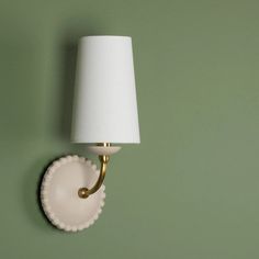 a wall light with a white shade on it's side against a green wall