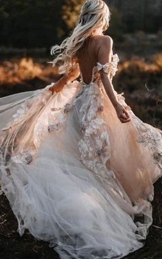 a woman in a wedding dress is walking through the grass with her back to the camera