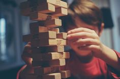 a young boy playing with wooden blocks in front of his face and hand on top of them