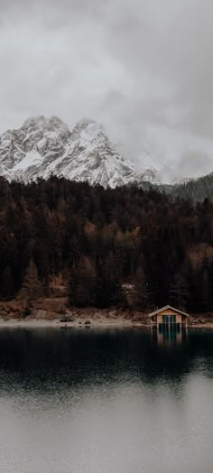 there is a boathouse on the water in front of a mountain with snow on it