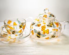 a glass tea set with yellow flowers and bees painted on the side, sitting on a table