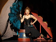 a woman in a black corset is holding a blue feathered umbrella and posing for the camera