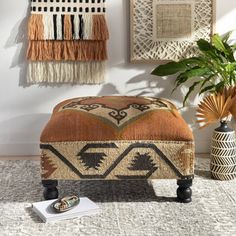 an orange ottoman sitting on top of a rug next to a potted plant and wall hangings